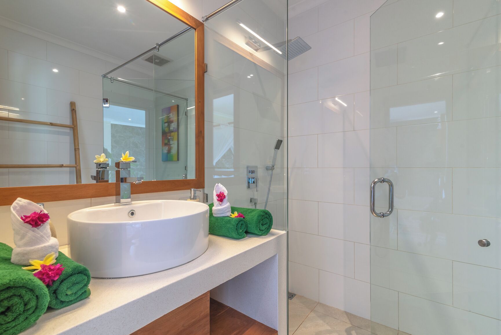 A modern bathroom with a large sink, a glass shower enclosure, and neatly rolled towels on the counter.