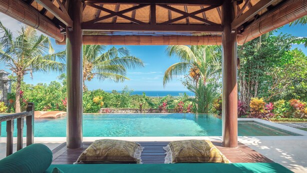 A poolside area with a view of the ocean, a covered seating area with cushions, and lush tropical vegetation. - Villa Mata Hari (Sukasada)