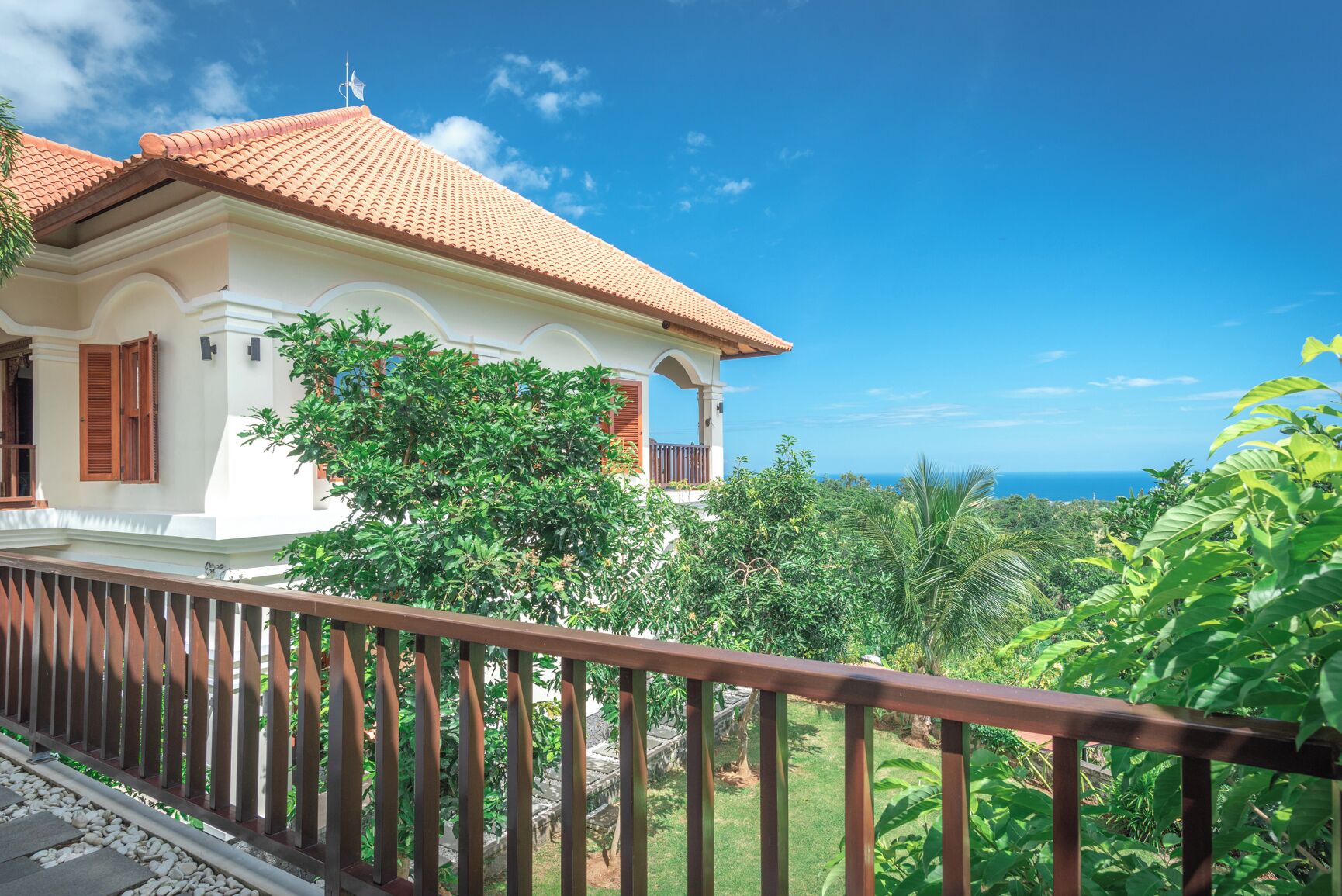 A white building with a red-tiled roof, surrounded by lush greenery and a clear blue sky.