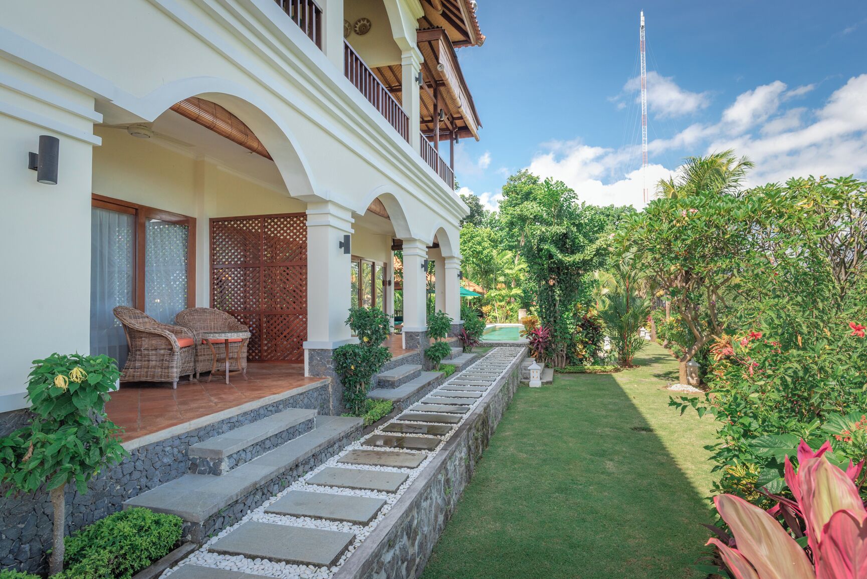 Un hotel con una zona de estar exterior cubierta, piscina y un jardín bien cuidado.