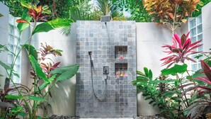 A shower area with a tiled wall, a handheld showerhead, and a small shelf with toiletries. - Villa Mata Hari (Sukasada)