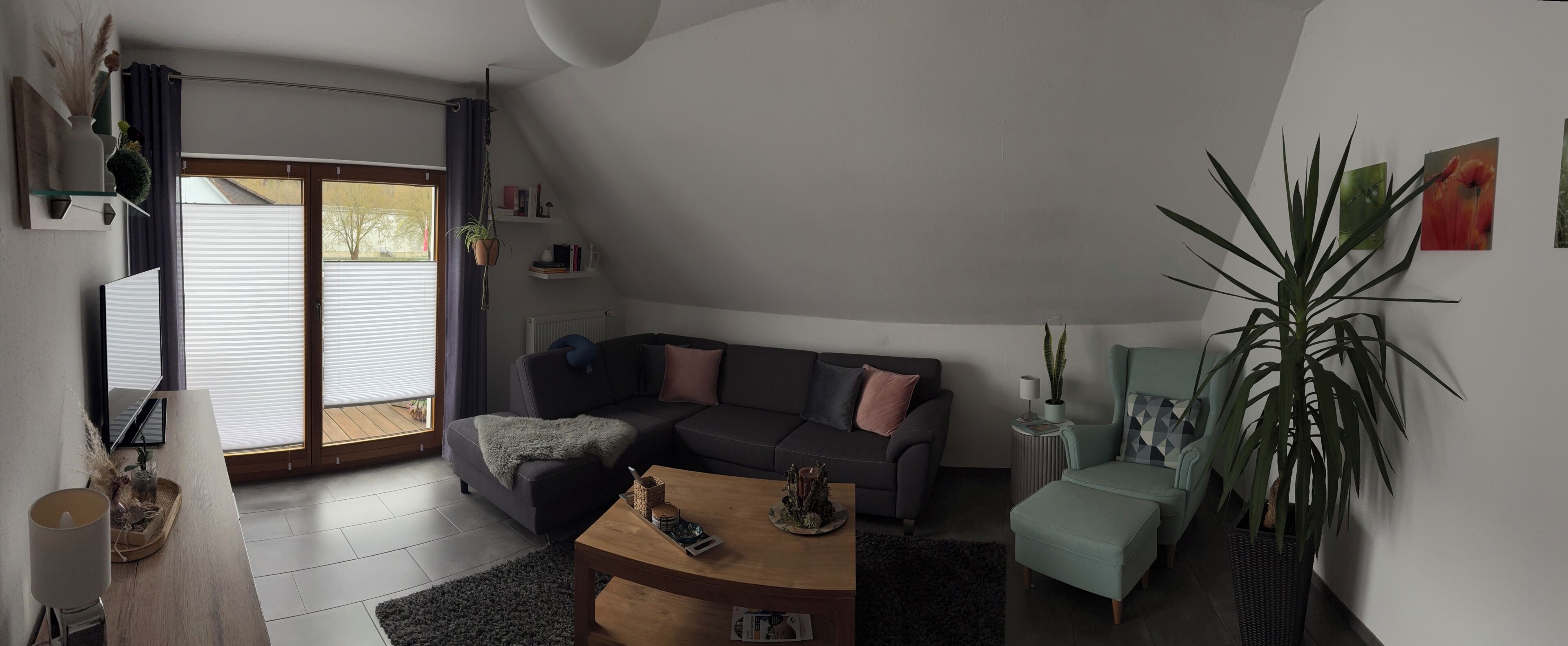 Een moderne woonkamer met een grijze bank, een houten salontafel, een bijzettafeltje en een grote potplant.