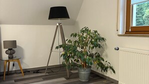 A room with a sloped ceiling, a potted plant, a floor lamp, and a window with blinds. - Comfortable vacation apartment in the center of Schleiden National Park (Schleiden)