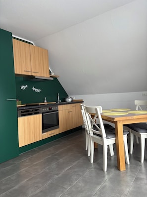 A compact kitchen with wooden cabinets, a built-in oven, and a dining area with a table and chairs. - Comfortable vacation apartment in the center of Schleiden National Park (Schleiden)