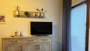 A living room with a wooden cabinet, a flat-screen TV, and a shelf with decorative items. - Comfortable vacation apartment in the center of Schleiden National Park (Schleiden)