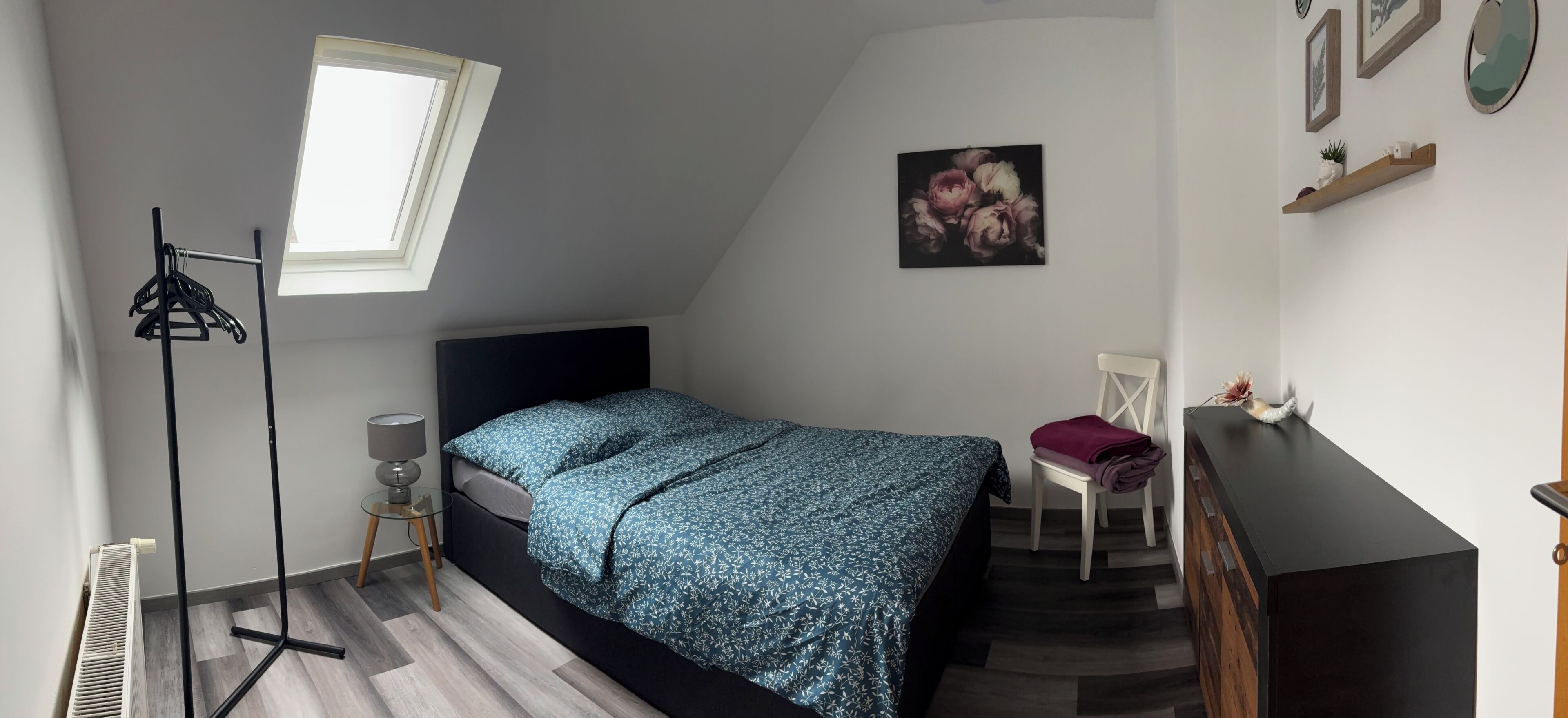 Un dormitorio con cama, escritorio, silla, radiador, lámpara colgante y ventana.