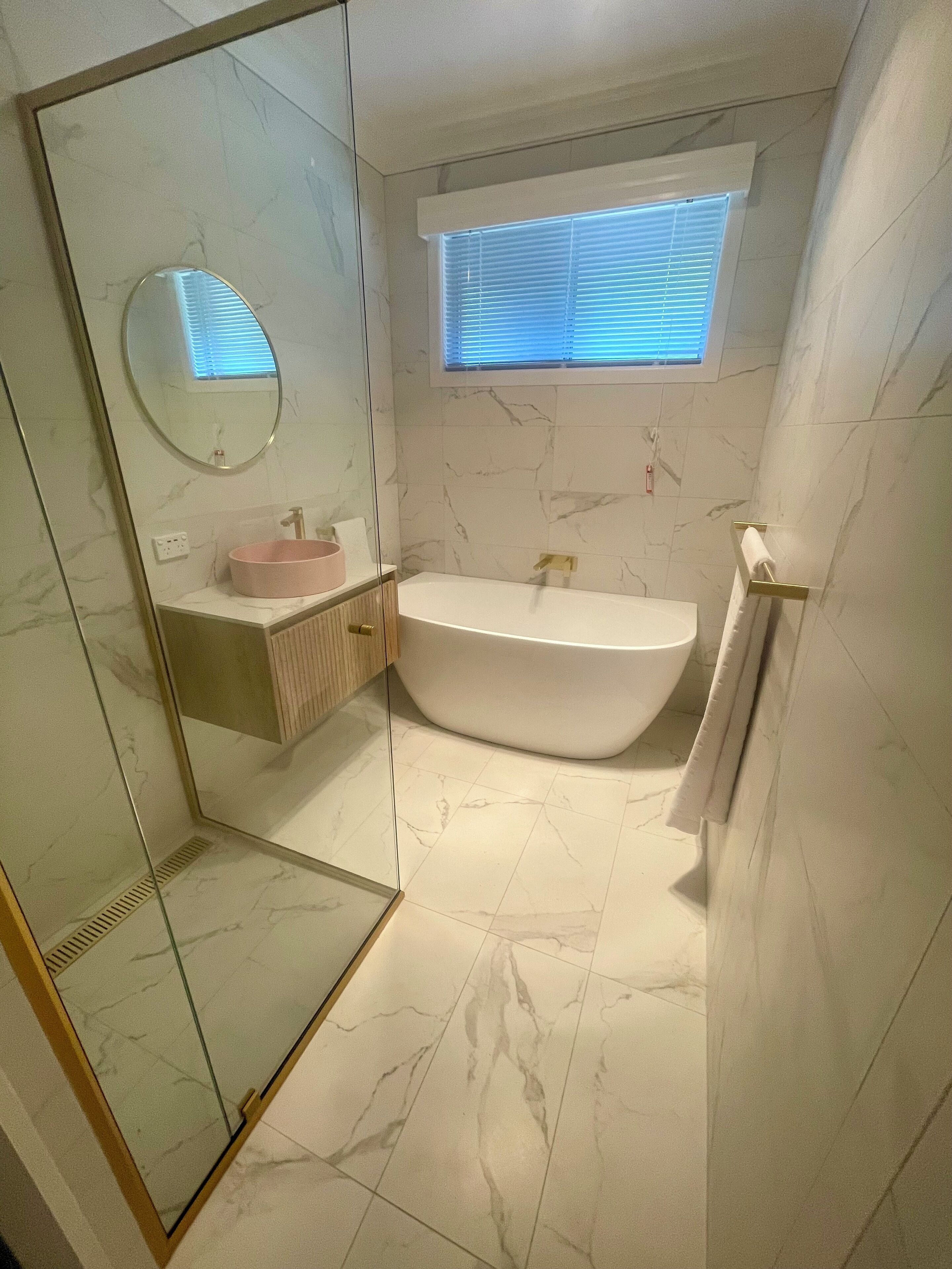 Ein modernes Badezimmer mit einer freistehenden Badewanne, einer Duschkabine aus Glas und einem Waschtisch mit einem rosa Waschbecken.
