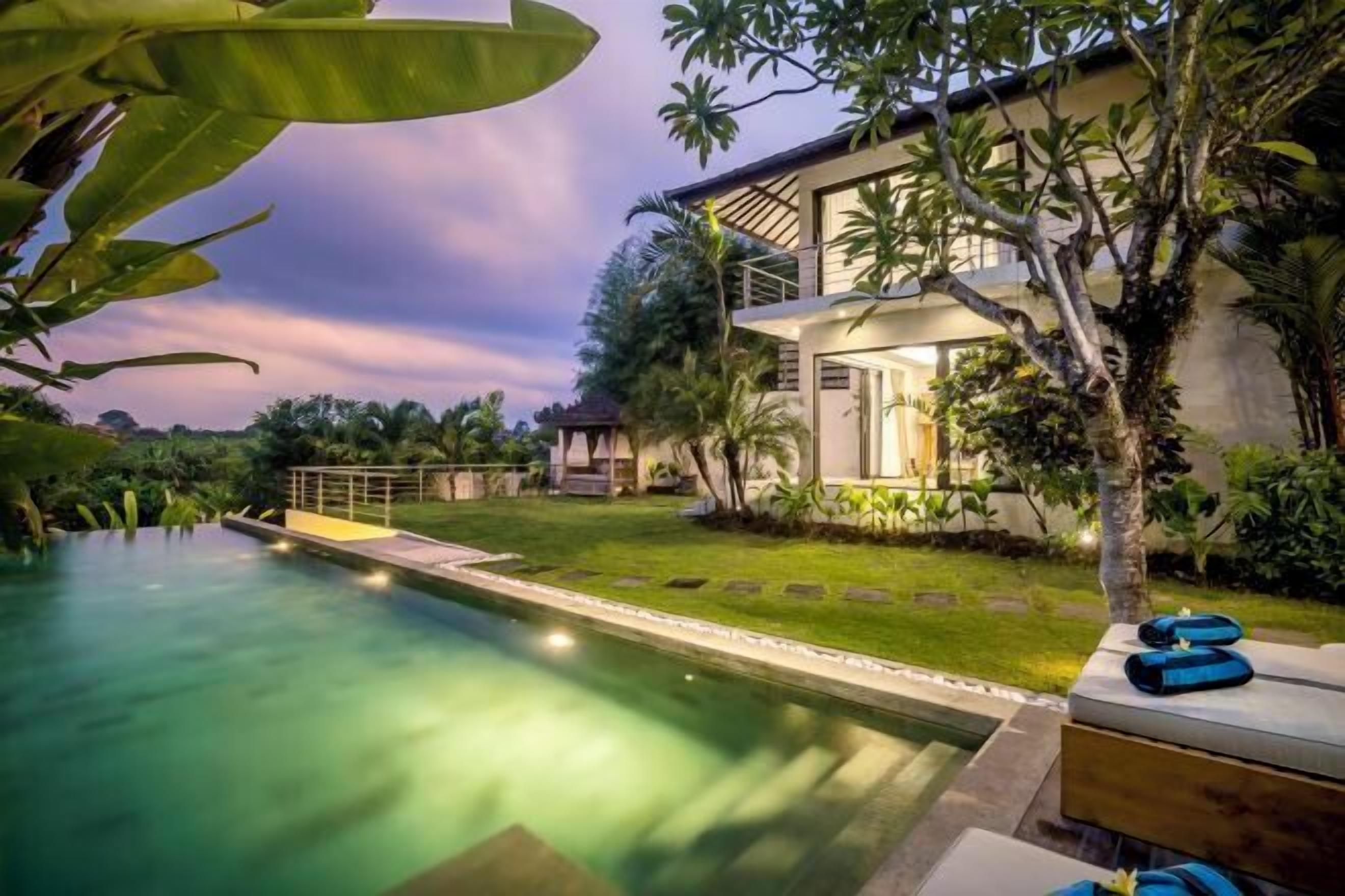 Una casa moderna con piscina, rodeada de exuberante vegetación y un césped cuidado.