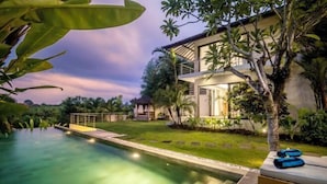 Una casa moderna con piscina, rodeada de exuberante vegetación y un césped cuidado.