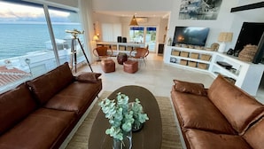 Ein modernes Wohnzimmer mit braunen Ledersofas, einem Couchtisch mit Pflanze und einem großen Fernseher.
