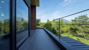 A modern balcony with a glass railing, offering a view of a lush green landscape and distant mountains. - Rinzan Chalet | 3BR Soga Chalet | Onsen-Style Bath & Yotei View (Rinzan)