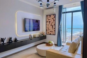 A modern living room with a large flat-screen TV, a sofa, a coffee table, and a view of the ocean through large windows. - Bap's House - CSJ Apartment Vung Tau (Vung Tau)
