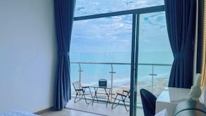A hotel room with a large bed, a view of the ocean through a sliding glass door, and a balcony with chairs and a table. - Bap's House - CSJ Apartment Vung Tau (Vung Tau)