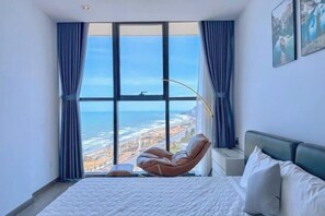 Une chambre avec une grande fenêtre, un lit, une chaise et une table de chevet.