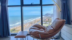 A room with a large window, a leather chair, and a small bench. - Bap's House - CSJ Apartment Vung Tau (Vung Tau)