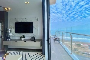 Une chambre moderne dotée d’une télévision, d’un mur en marbre et d’un balcon offrant une vue sur l’océan.