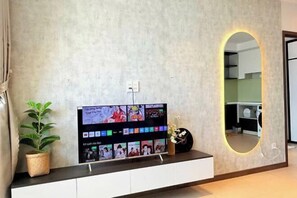 Un salon moderne avec un téléviseur à écran plat fixé à un mur texturé, une plante en pot et un miroir décoratif agrémenté d’un éclairage néon.