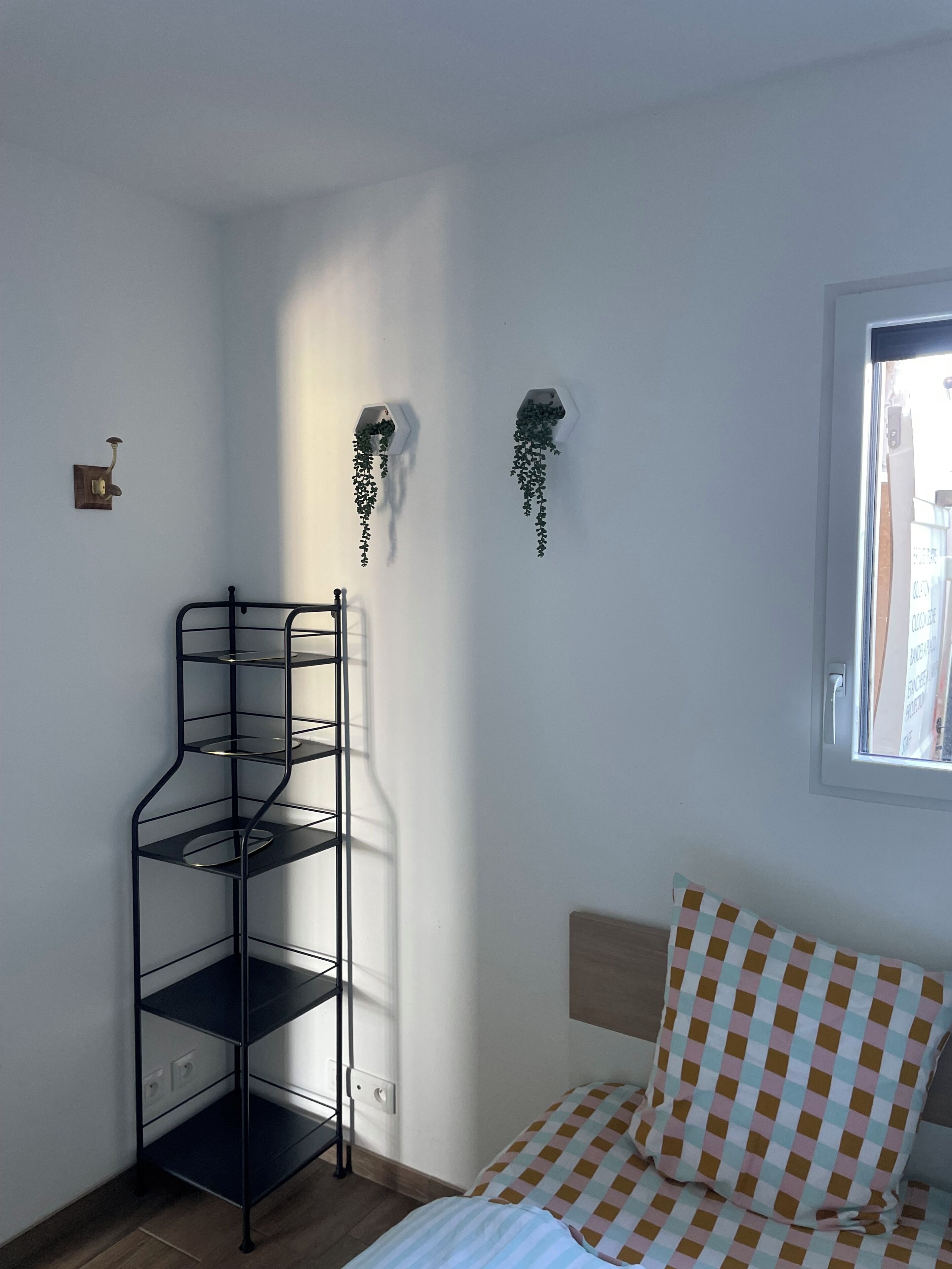 Une chambre avec un lit, une étagère en métal noir et deux jardinières fixées au mur.