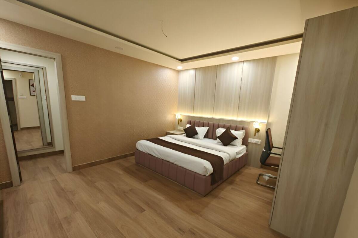 Una habitación de hotel moderna con una cama grande, suelo de madera, cabecero incorporado y un espejo en la pared izquierda.