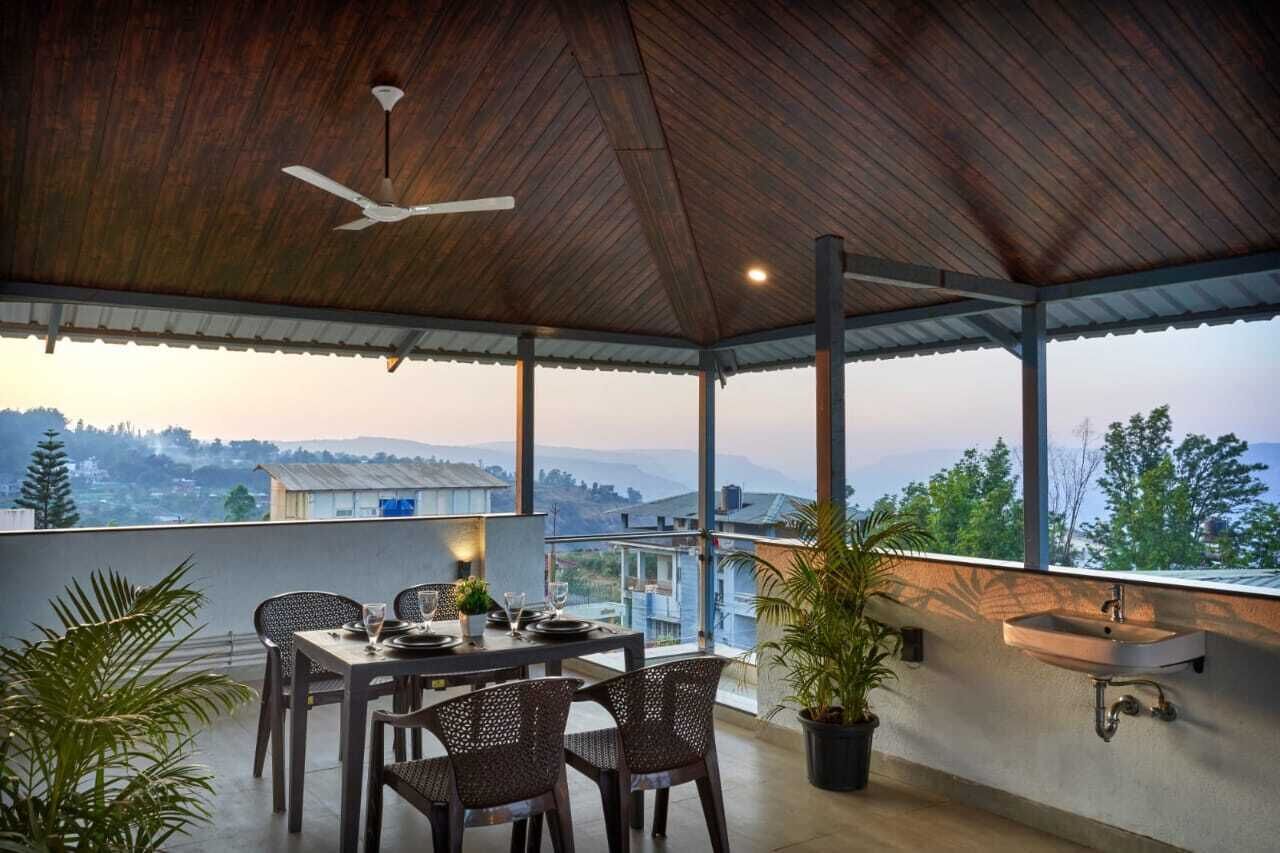 A covered outdoor dining area with a table and chairs, a ceiling fan, and a view of the surrounding landscape.
