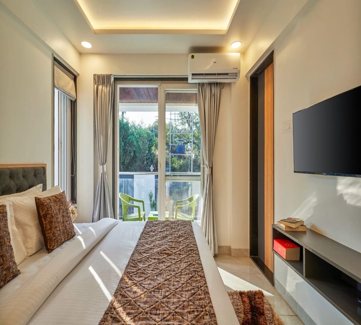 A modern bedroom with a large bed, a flat-screen TV, and a balcony with a view of greenery.