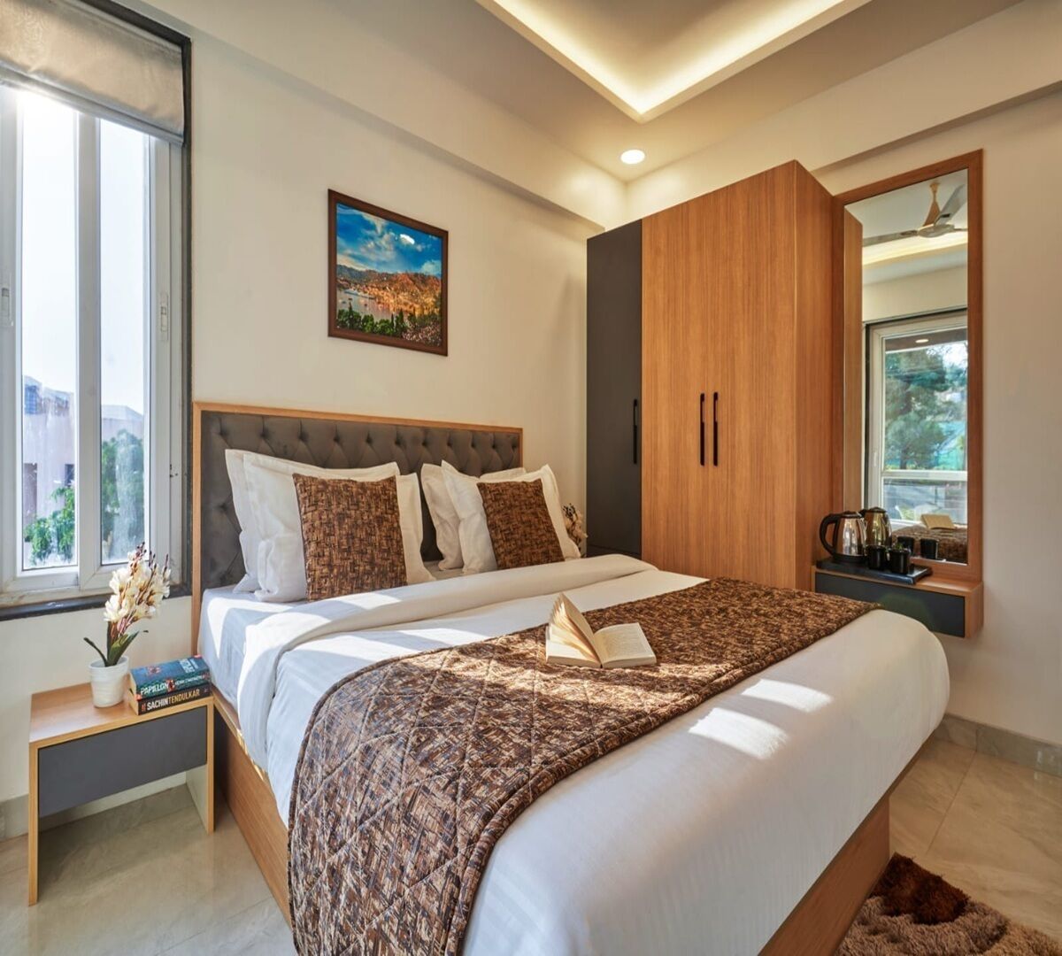 A modern bedroom with a large bed, a nightstand, a wooden wardrobe, a window with a city view, and a painting on the wall.