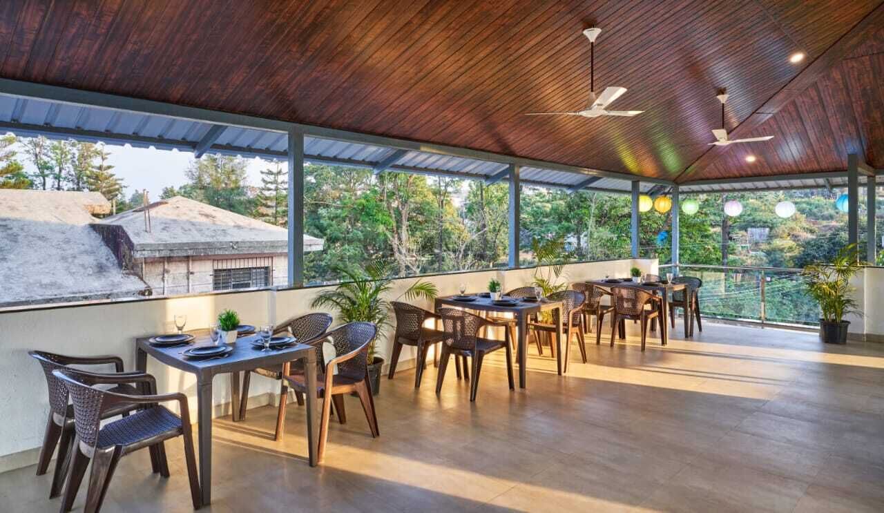 Un área de comedor al aire libre con mesas y sillas de madera, ventanas amplias y ventiladores de techo.