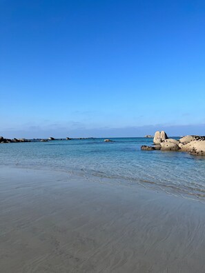A beach with clear water, sandy shore, and large rocks.