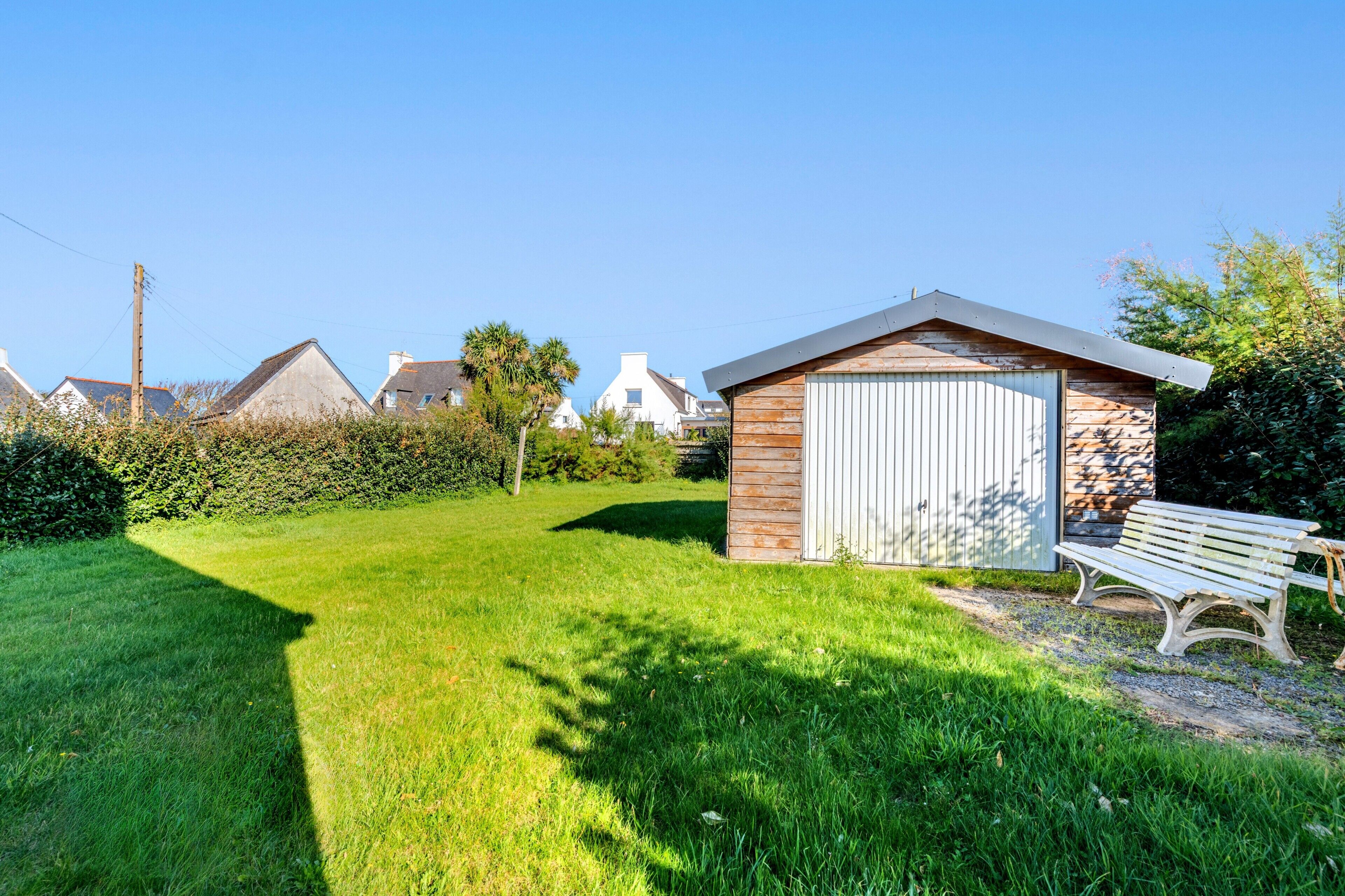 A small wooden shed with a white door, a bench, and a well-maintained lawn in a residential area.