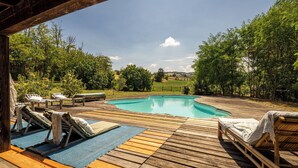 Una terraza de madera con piscina, sillas de descanso y vistas a un paisaje verde.