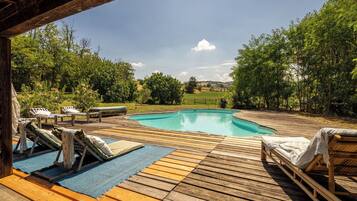 Un pontile di legno con piscina, sedie a sdraio e vista su un paesaggio verde.