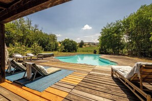 Una terraza de madera con piscina, sillas de descanso y vistas a un paisaje verde.