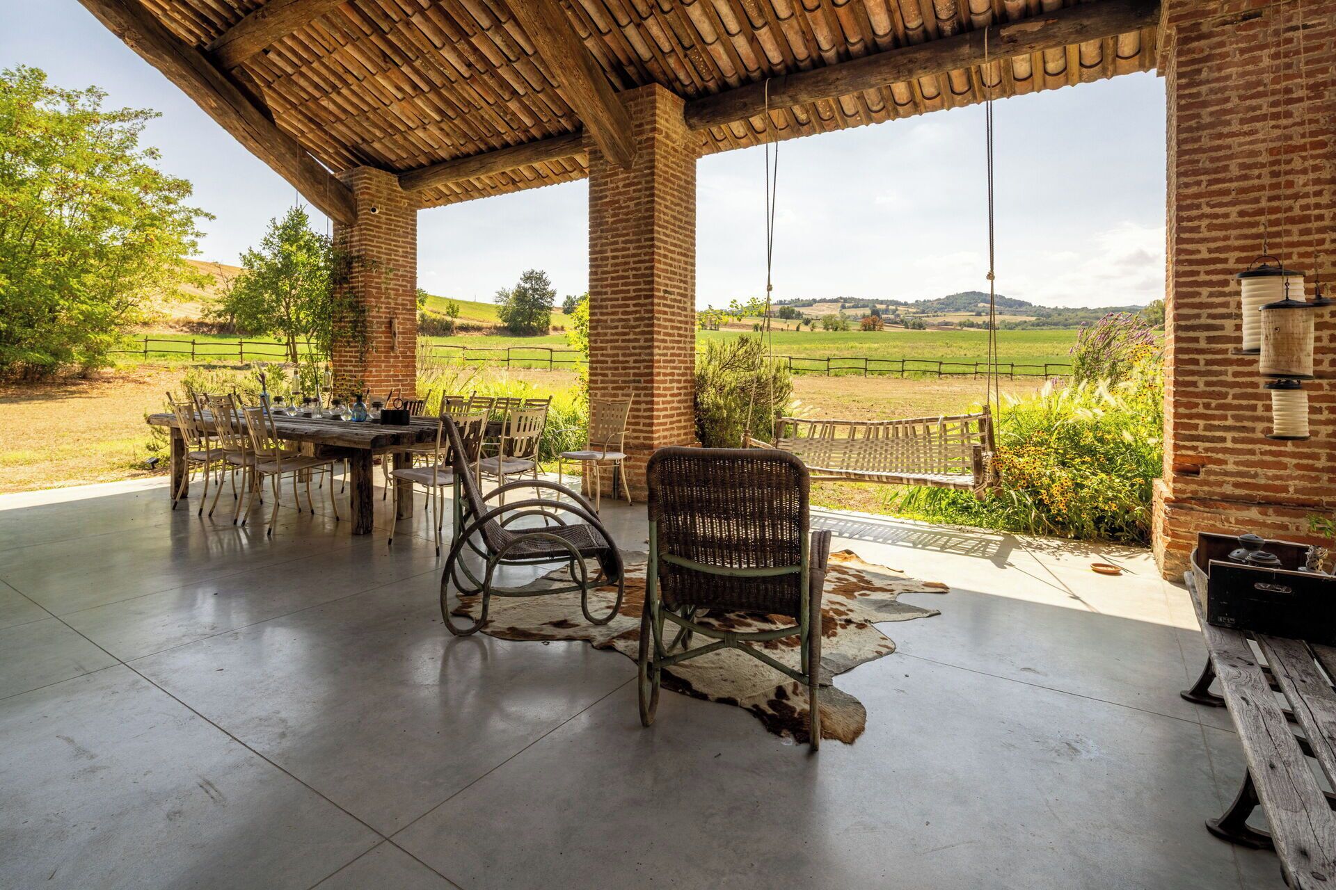 Un patio exterior con pared de ladrillo, mesa de madera y sillas de mimbre.