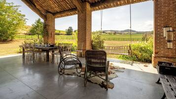 Una terrazza esterna con un muro in mattoni, un tavolo di legno e sedie in vimini.