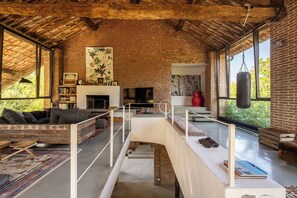 Amplia sala de estar con chimenea de ladrillo, televisor y ventana grande con vistas a zonas verdes.