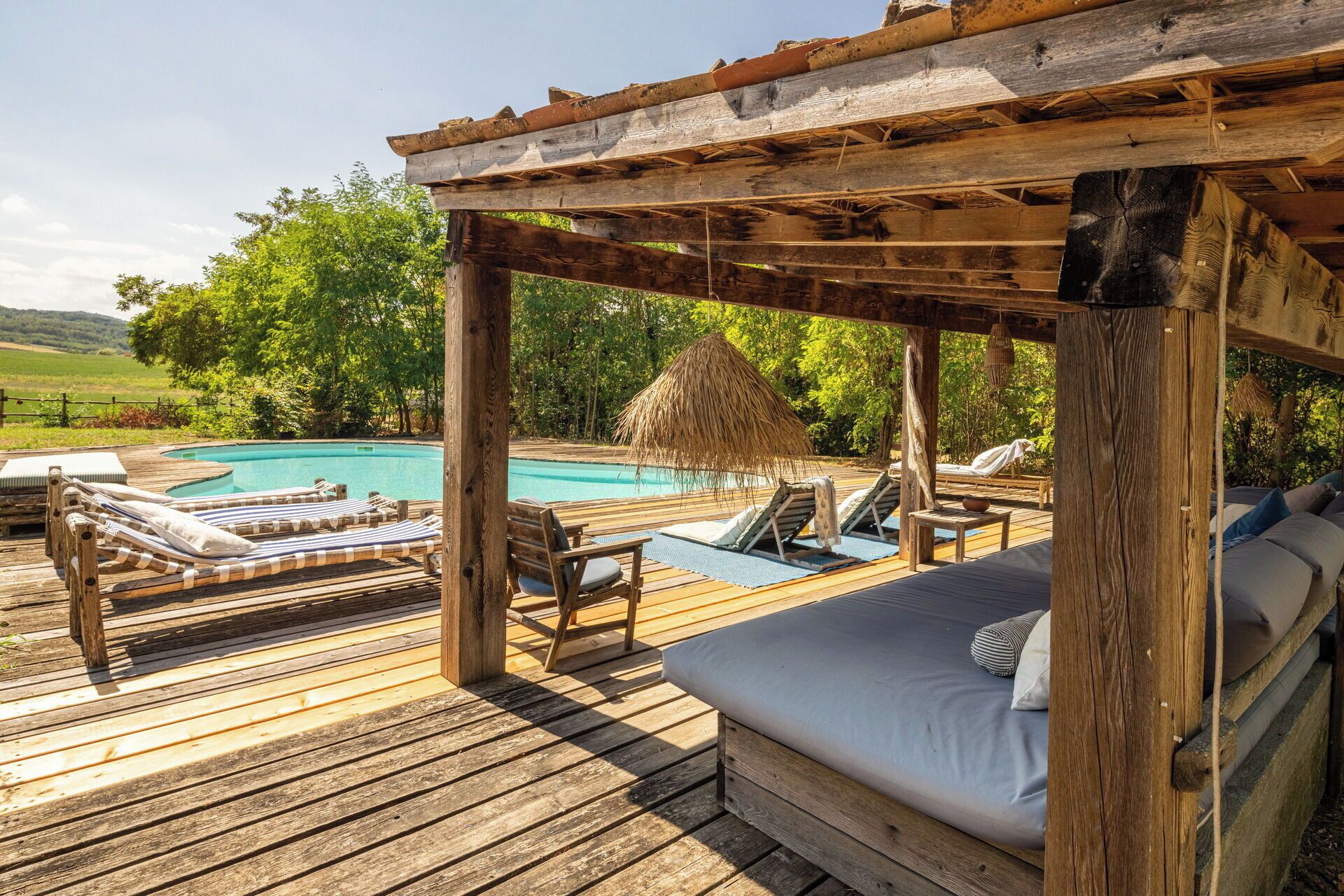 Une terrasse en bois avec une piscine, des chaises longues et un espace salon abrité.