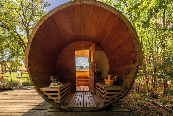 Una cabaña de madera con entrada circular, una terraza de madera exterior y vistas del bosque circundante.
