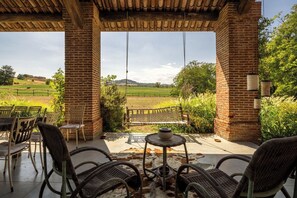 A covered outdoor seating area with brick pillars, wicker chairs, and a view of a green field.