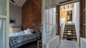 Un dormitorio con cama, ventana con cortinas, pared de ladrillo y escalera de madera.