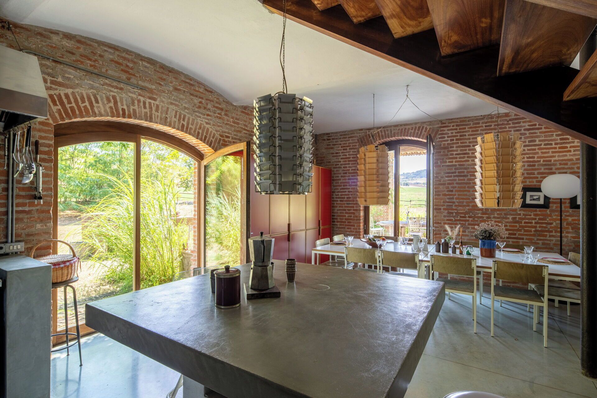 Une cuisine spacieuse dotée d’un grand îlot central, de murs en briques et de grandes fenêtres offrant une vue sur la verdure.