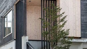 Un edificio con fachada de madera, barandilla negra y un árbol en frente.