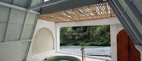 Un espace de bien-être comprenant un jacuzzi, une porte en bois et donnant sur un jardin.