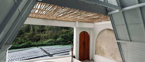 Un espace spa moderne doté d’un jacuzzi, d’une porte en bois et offrant une vue sur un toit à travers une structure en verre.