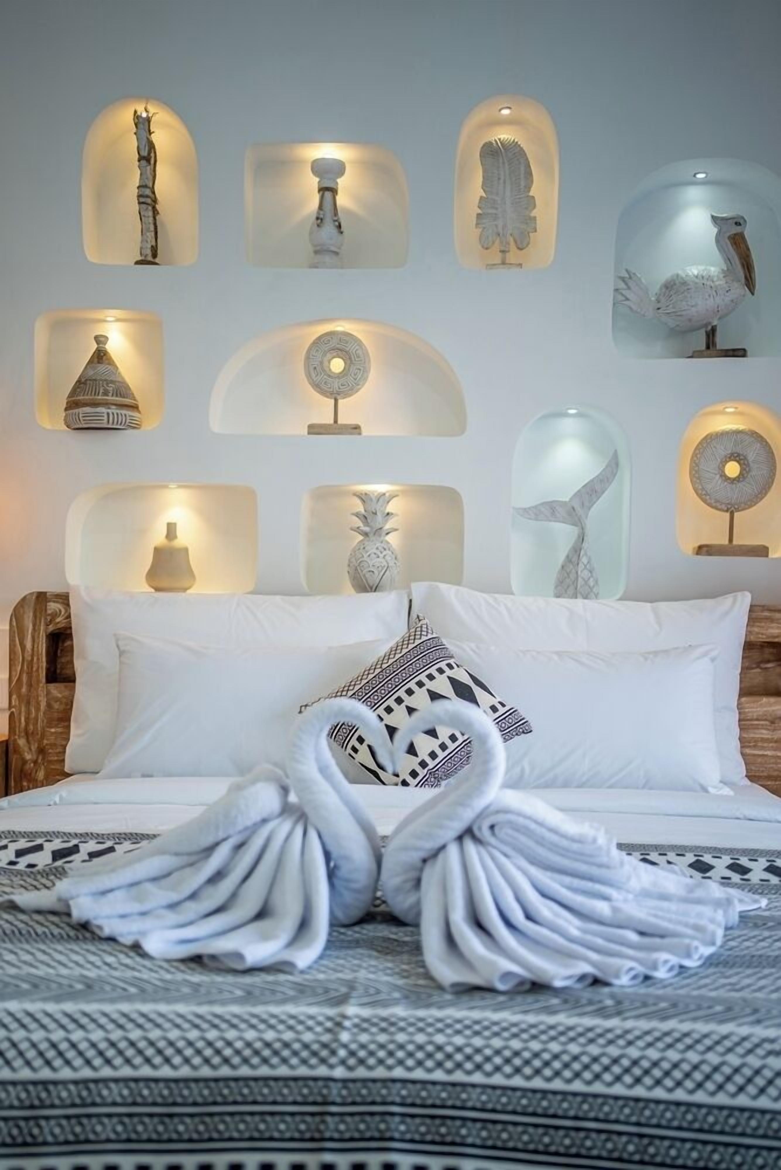 A bed with a swan-shaped towel, white pillows, and a patterned bedspread.
