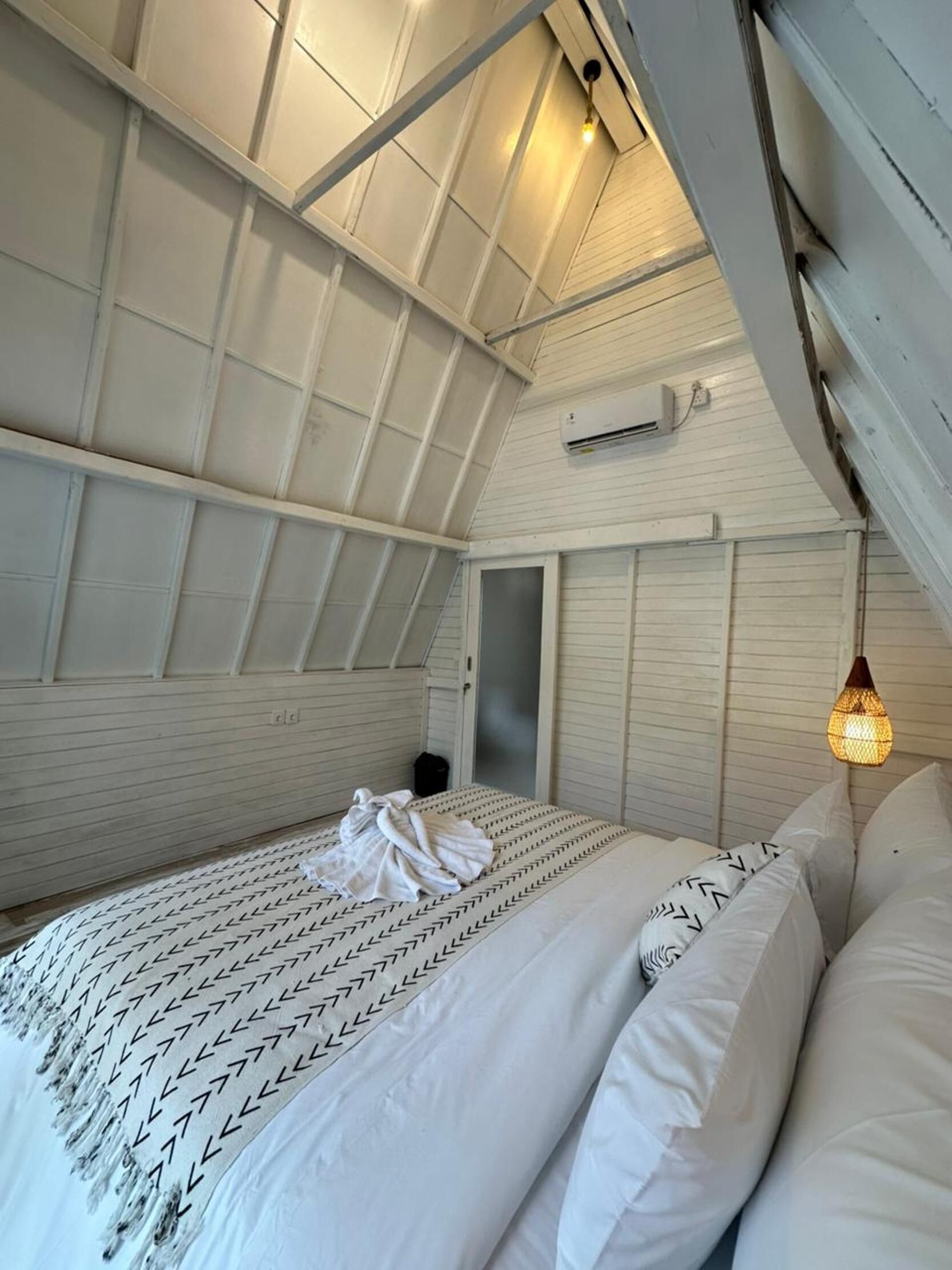 A bedroom with a sloped ceiling, a bed with patterned bedding, and a hanging light fixture.