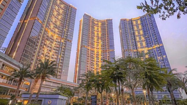 Un edificio residencial alto con varios balcones, rodeado de vegetación y palmeras.