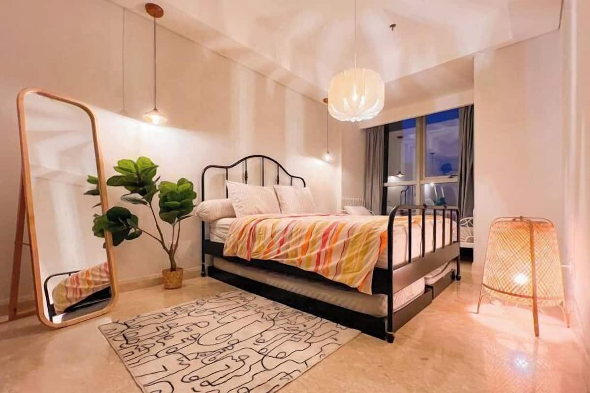 Een moderne slaapkamer met een bed, een grote spiegel, een potplant en een hanglamp.