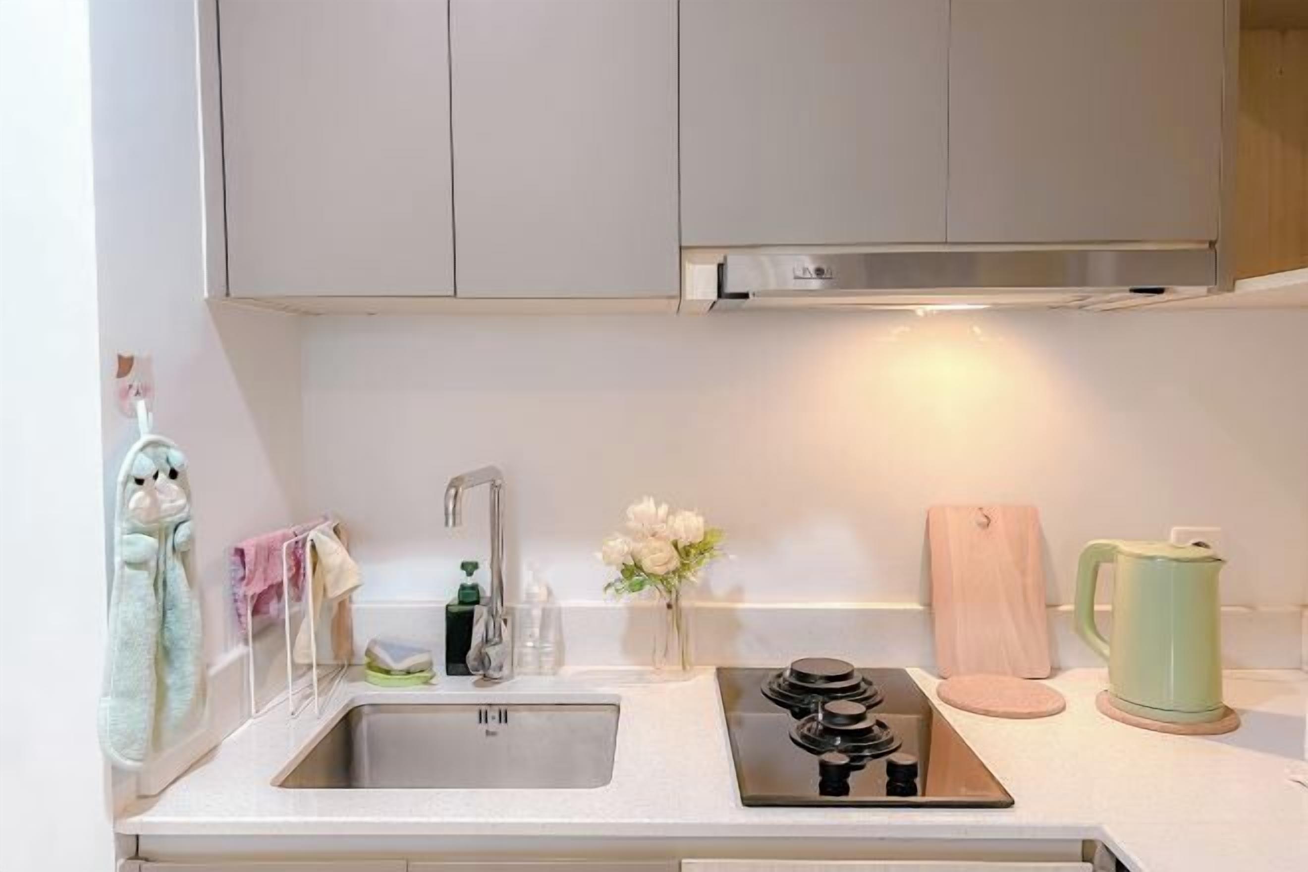 A kitchen with a stainless steel sink, a stove, a wooden cutting board, and a green kettle.