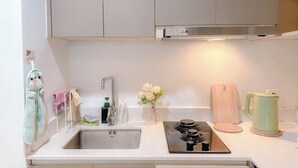 Una cocina con un lavamanos de acero inoxidable, una estufa, una tabla de cortar de madera y un hervidor verde.