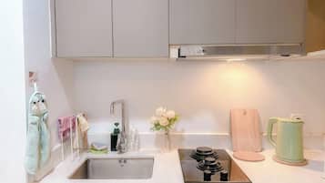 A kitchen with a stainless steel sink, a stove, a wooden cutting board, and a green kettle.